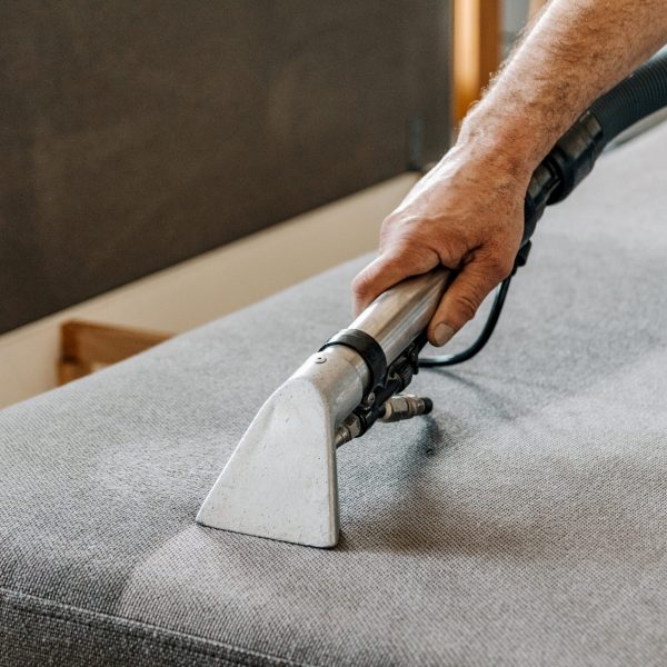 Man holding professional deep clean machine and cleaning couch in living room in apartment.